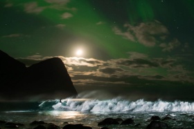 极光下在挪威荒芜的海滩冲浪
